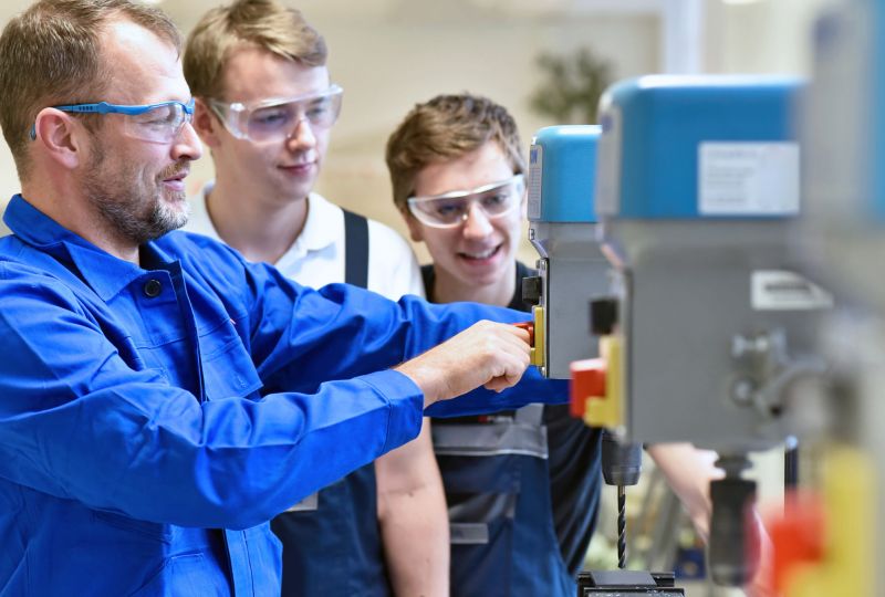 Group of young people in mechanical vocational training with teacher at drilling machine